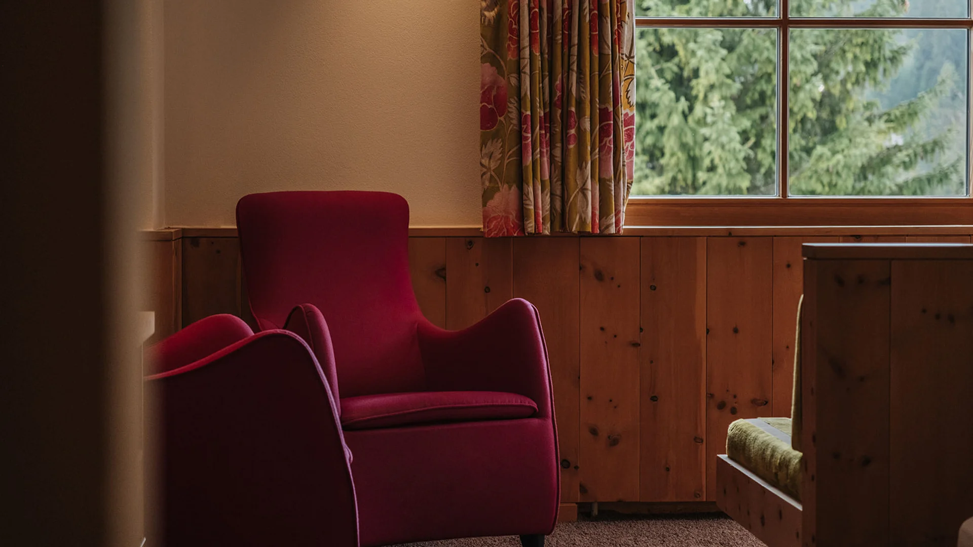 Roter Sessel vor einem Fenster mit Blick auf grüne Bäume in einem Raum mit Holzvertäfelung