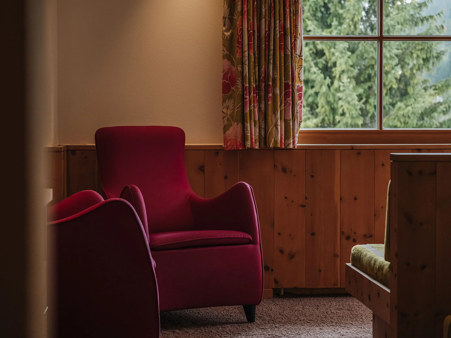 Red armchair by a window overlooking green trees in a wood-paneled room