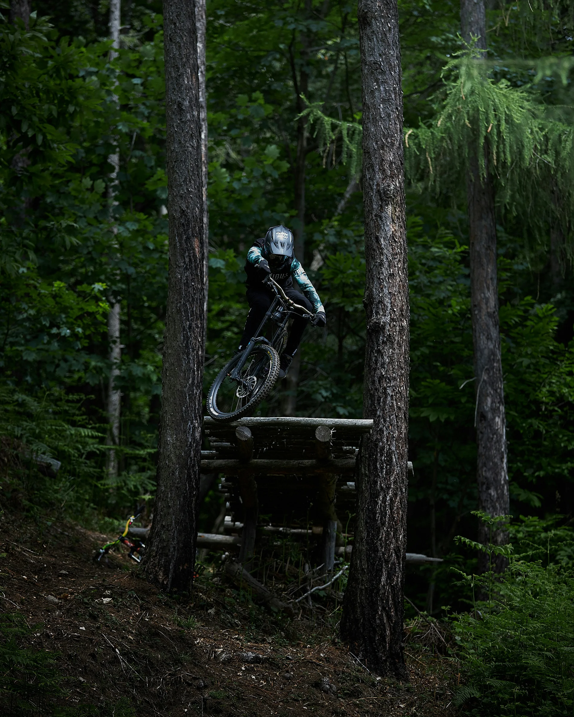 Mountain biker jumping off wooden ramp in dark forest