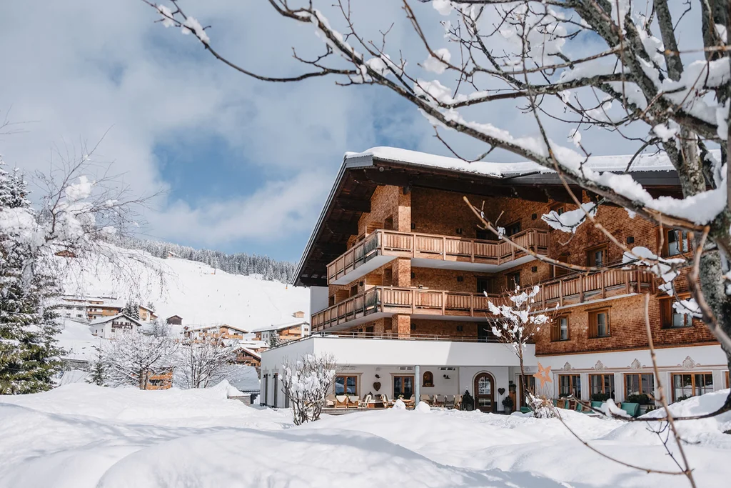 Verschneites Hotelgebäude mit Balkon in einer winterlichen Alpenlandschaft