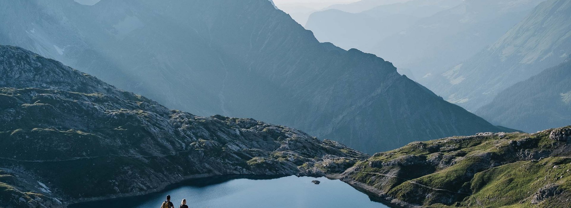 Kleine Wandergruppe genießt den Ausblick auf einen See mit der Berglandschaft im Hintergrund.