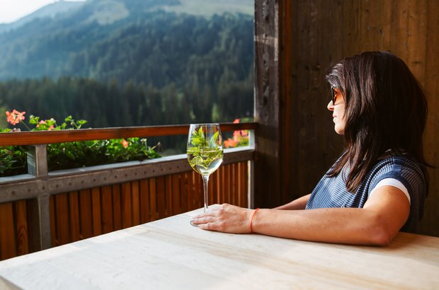 Braunarl Balkon Frau sitzt mit einem erfrischendem Getränk in der Sonne.
