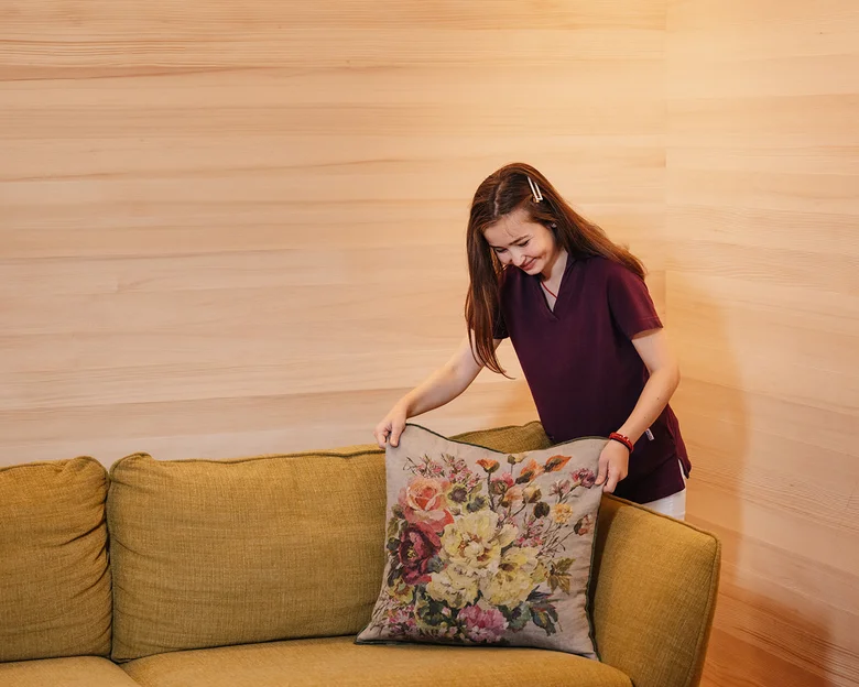 Das Team des Hotel Aurora in Lech Frau legt Kissen mit Blumenmuster auf grünes Sofa in hellem Raum