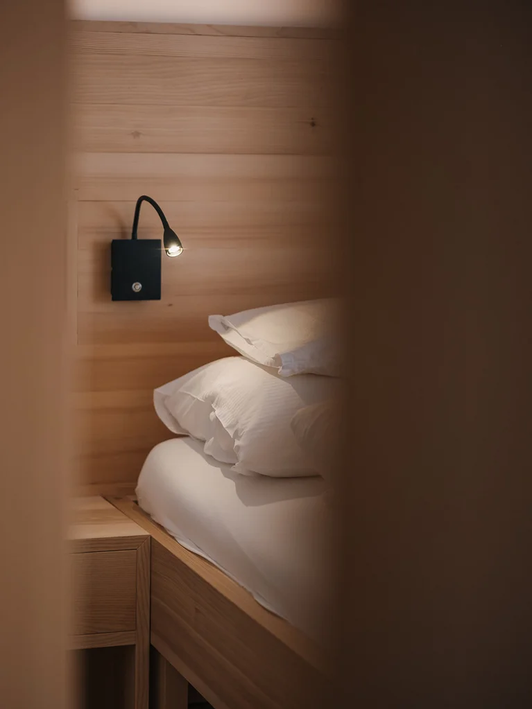 Gemütliches Bett mit Leselampe an Holzwand