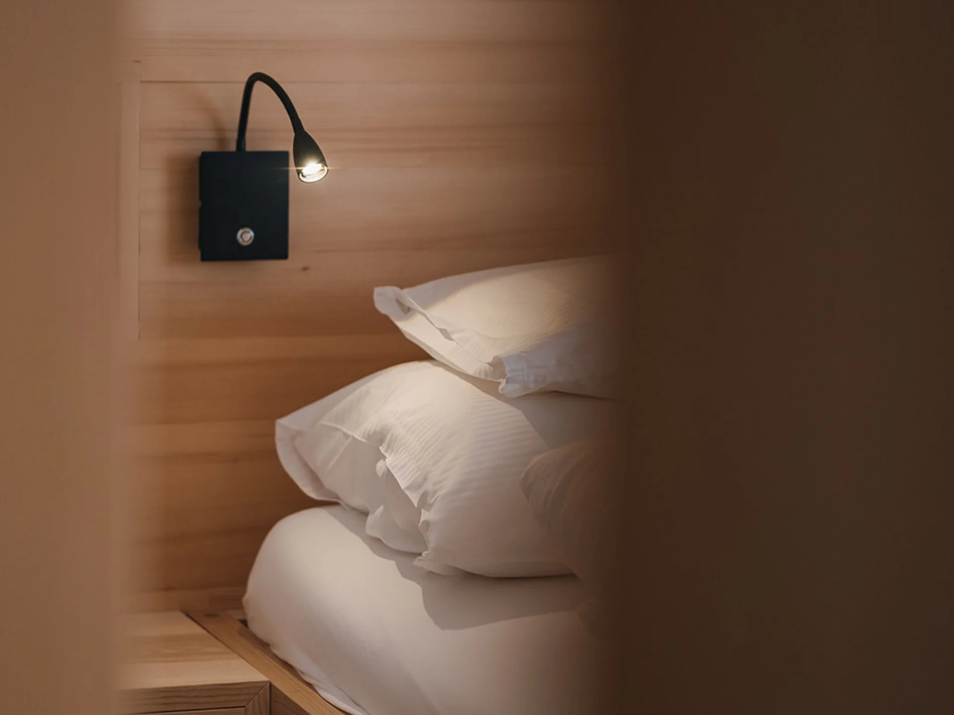 Cozy bed with reading lamp on wooden wall