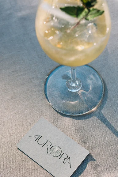 Cocktailglas mit einer Minze und eine Visitenkarte mit dem Logo Aurora