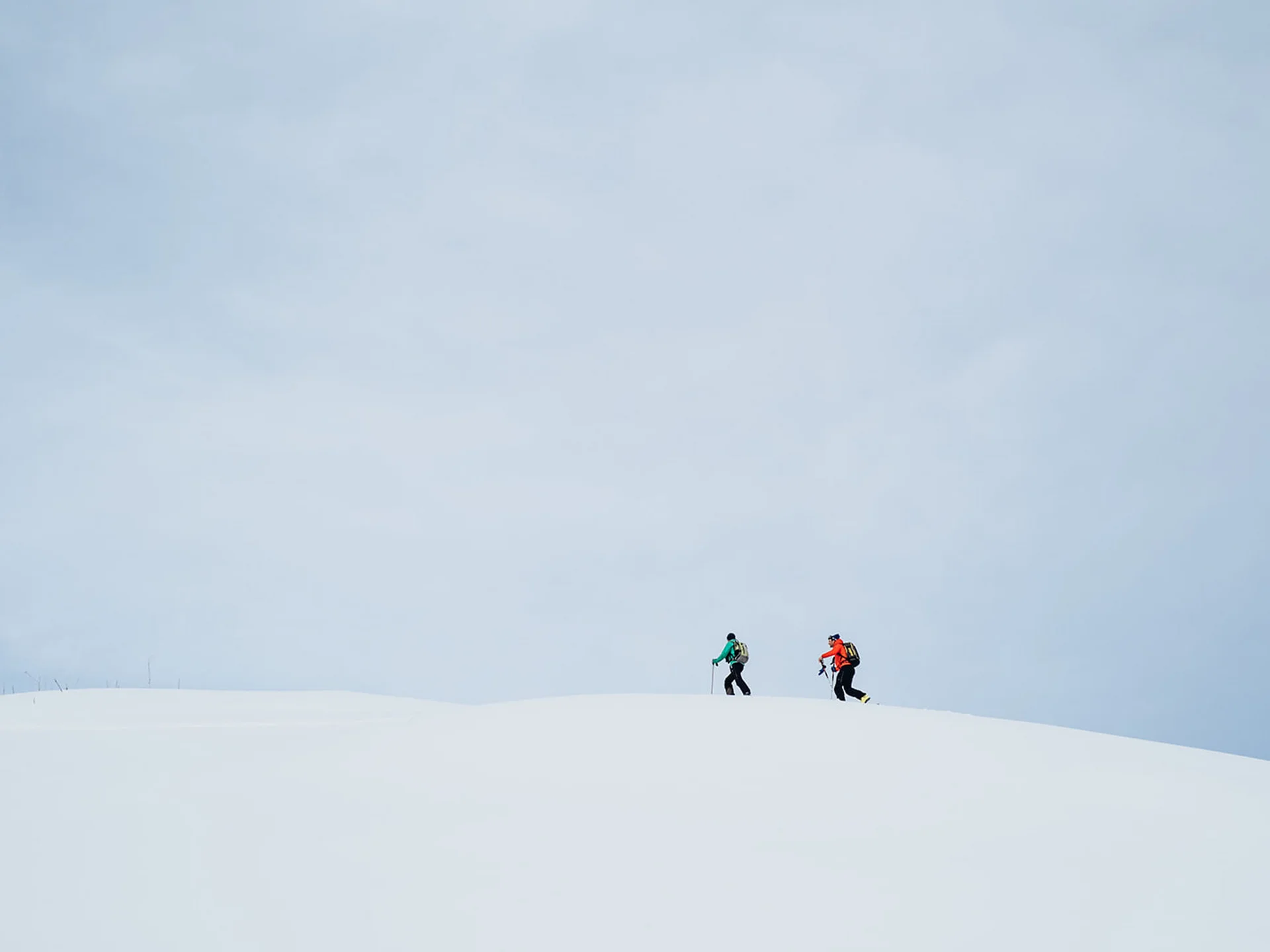 Two people hiking with ski poles on snowy hill under cloudy sky