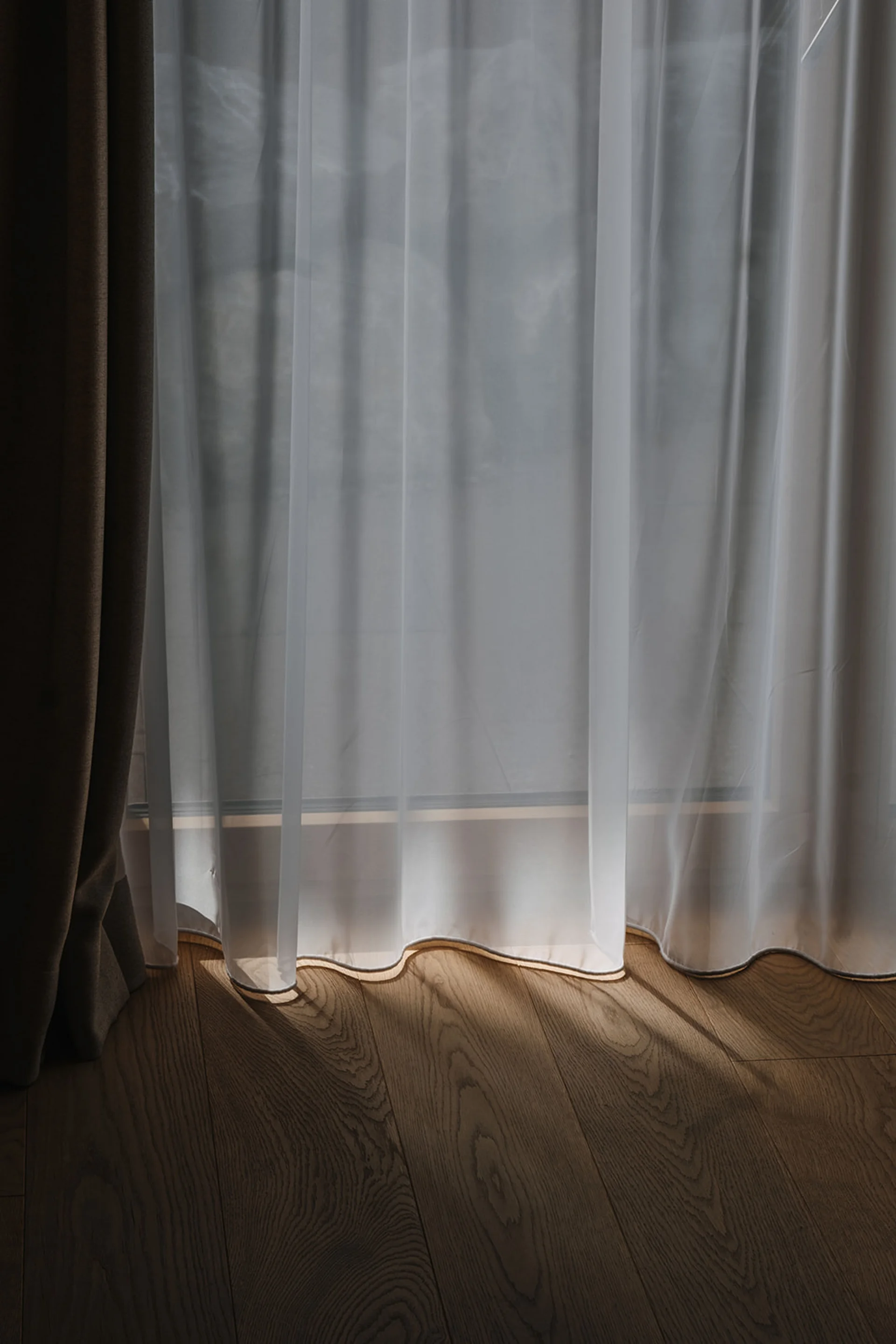 Sonnenschein scheint durch einen weißen transparenten Vorhang auf einen hölzernen Boden
