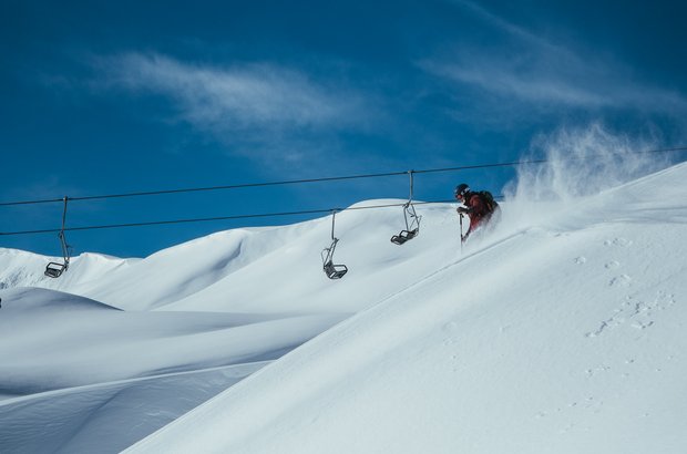 Mann fährt über die Piste und man sieht einen Sessellift im Hintergrund.