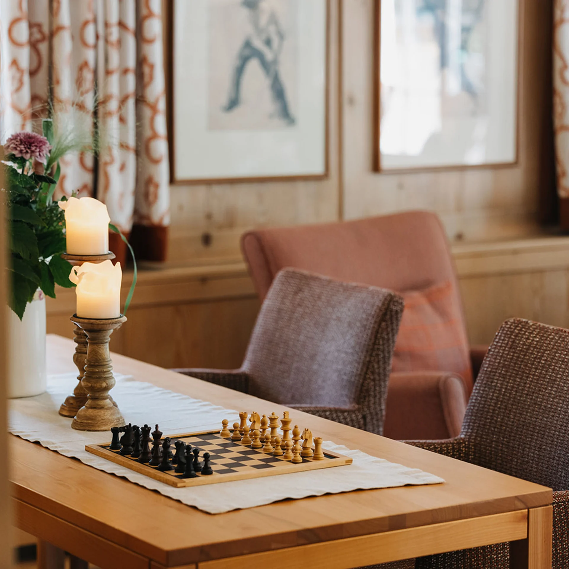 Gemütlicher Raum mit Schachbrett, Kerzen und Sessel an Holztisch