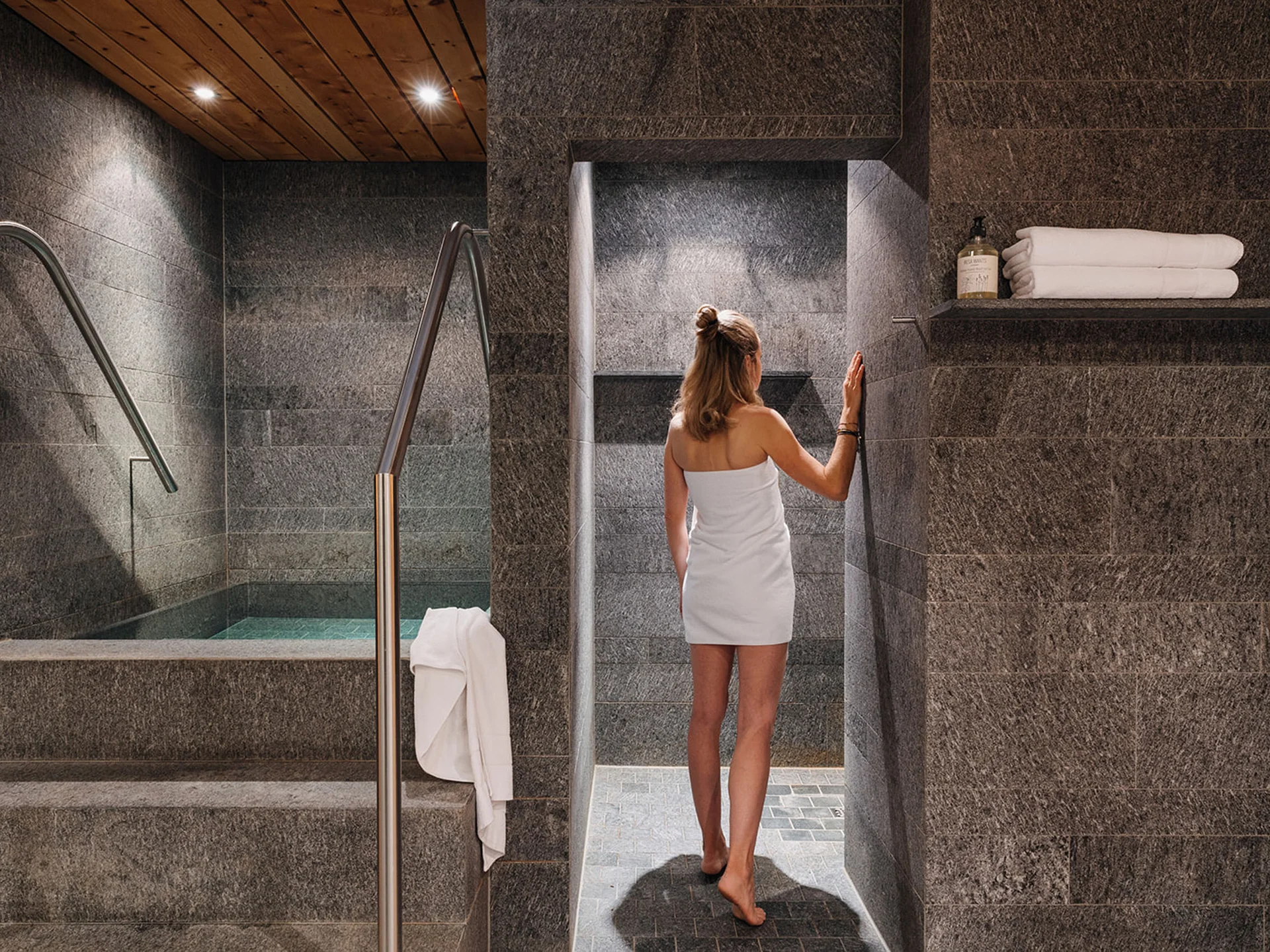 Woman in towel entering spa area with stone walls and steam room