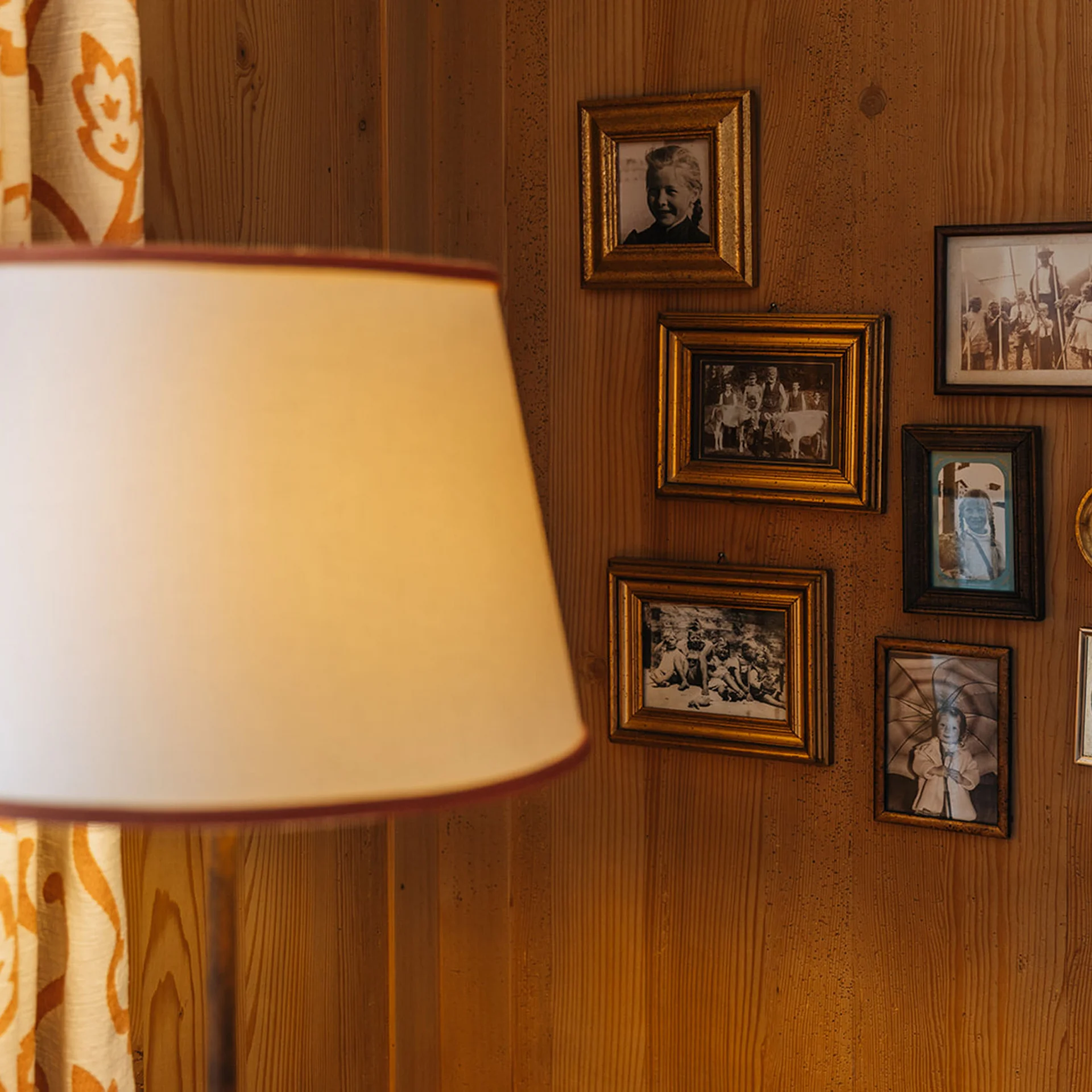 Stehlampe vor einer Holzwand mit mehreren alten Familienfotos in Rahmen