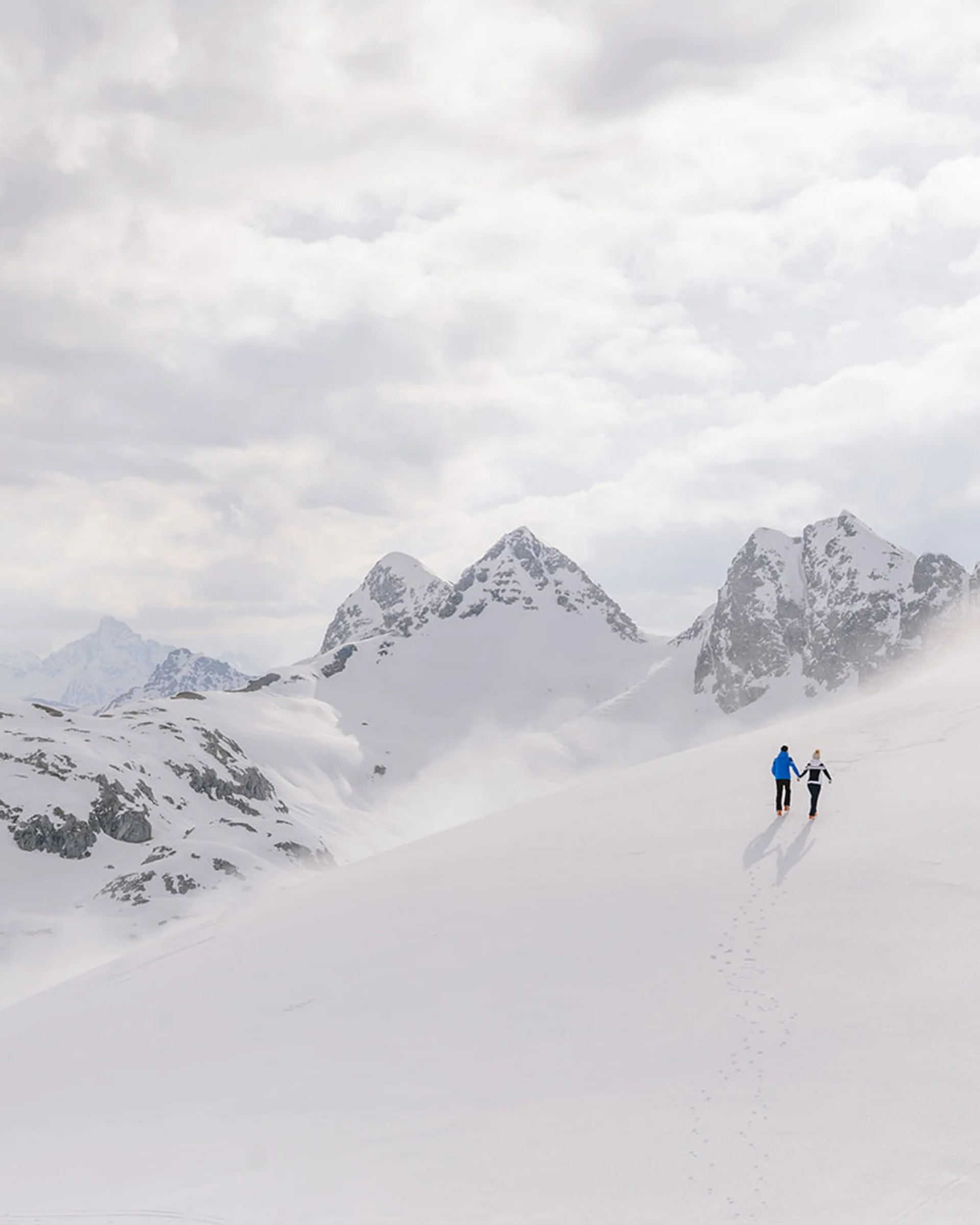 Zwei Personen gehen im Schnee auf einem Berg bei bewölktem Himmel