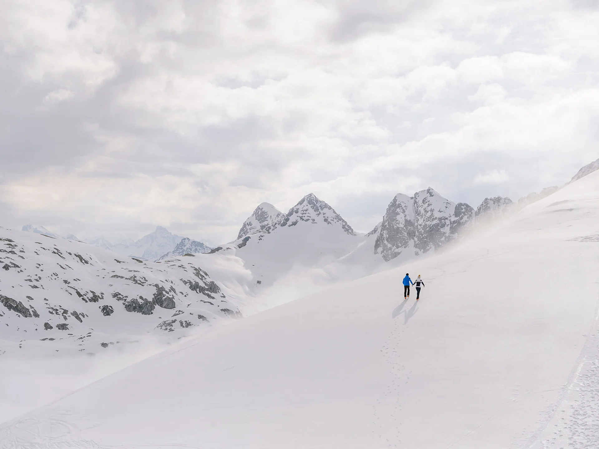 Two people walking in the snow on a mountain under cloudy sky