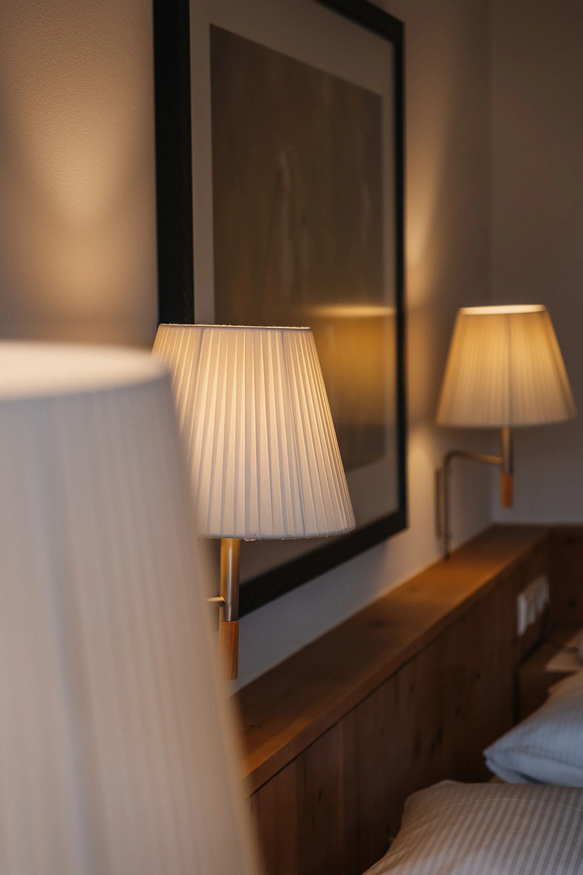 Beleuchtete Wandlampen über einem hölzernen Bettrahmen in einem Schlafzimmer