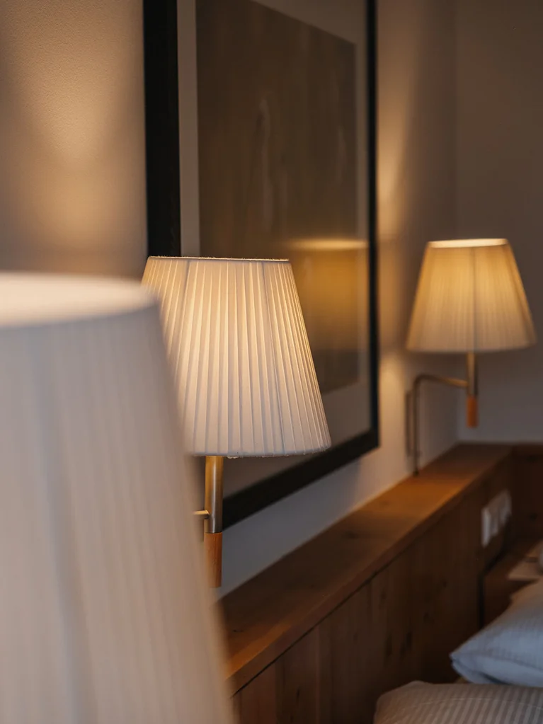 Beleuchtete Wandlampen über einem hölzernen Bettrahmen in einem Schlafzimmer