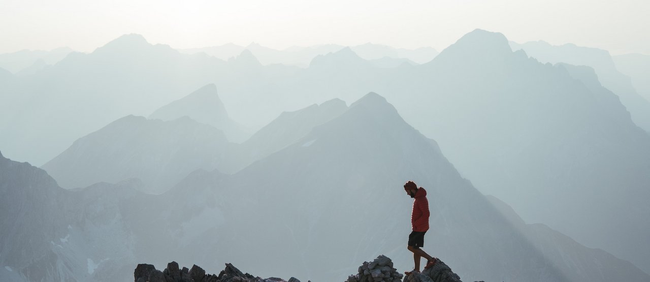 Mann wandert über schroffes Gestein vor einem atemberaubendem Bergpanorama.