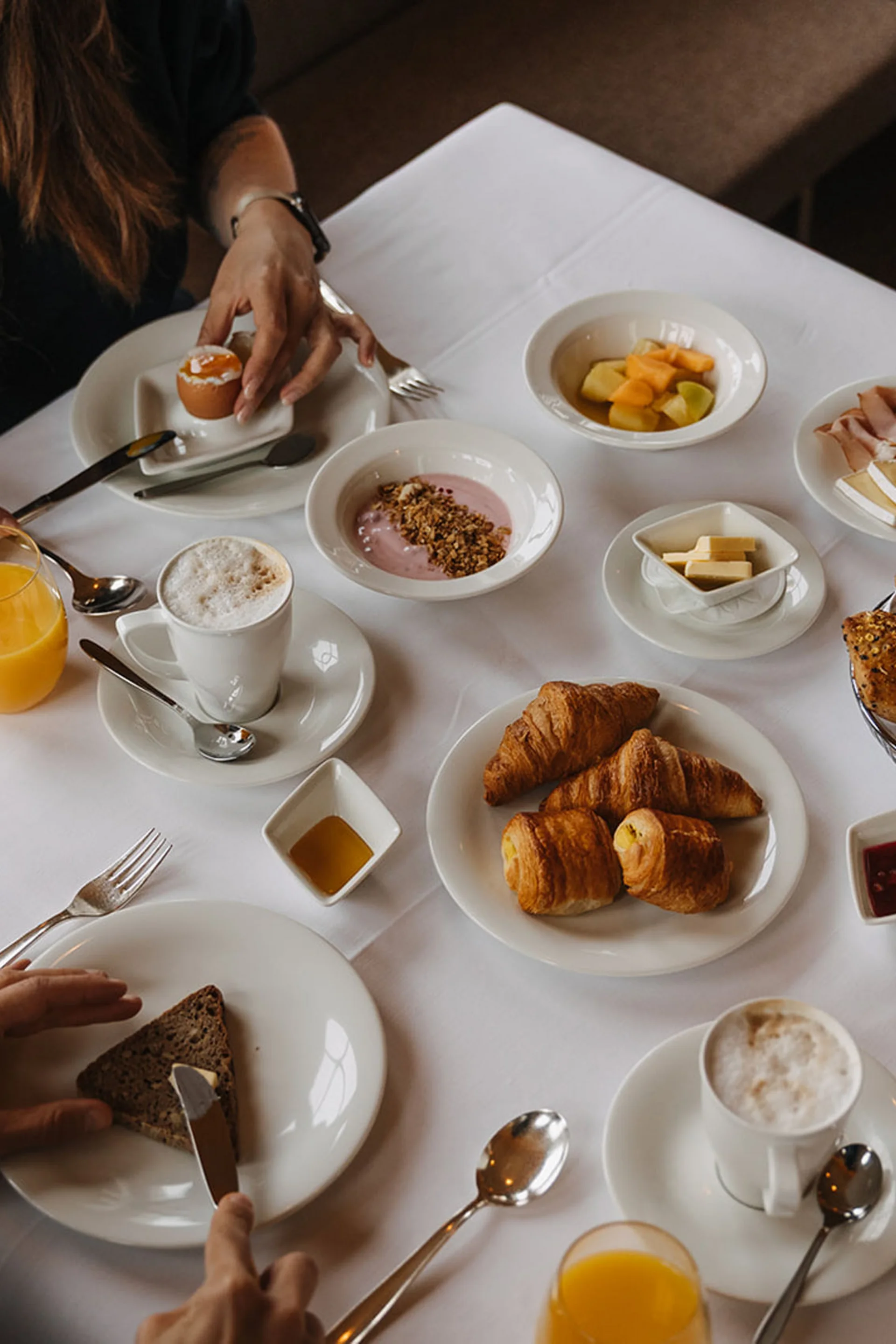 Frühstückstisch mit Croissants, Eiern, Kaffee, Orangensaft und Aufschnitt