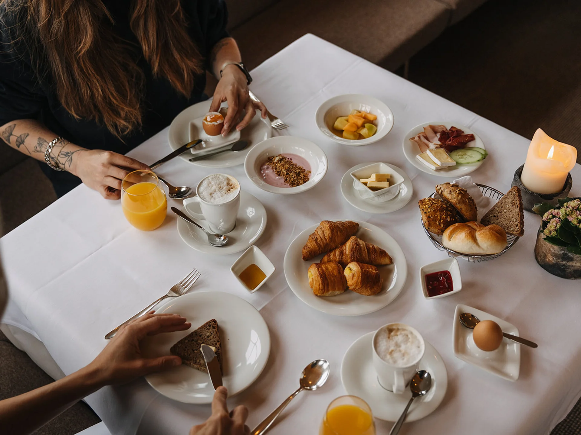 Breakfast table with croissants, eggs, coffee, orange juice, and cold cuts