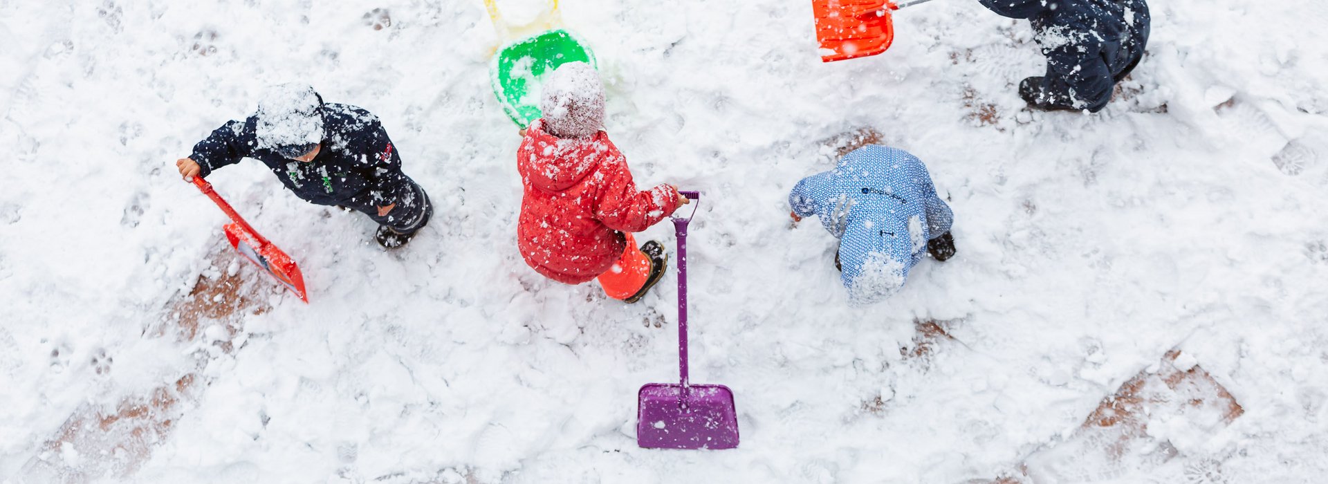 Kinder spielen im Schnee mit Schneeschippen.
