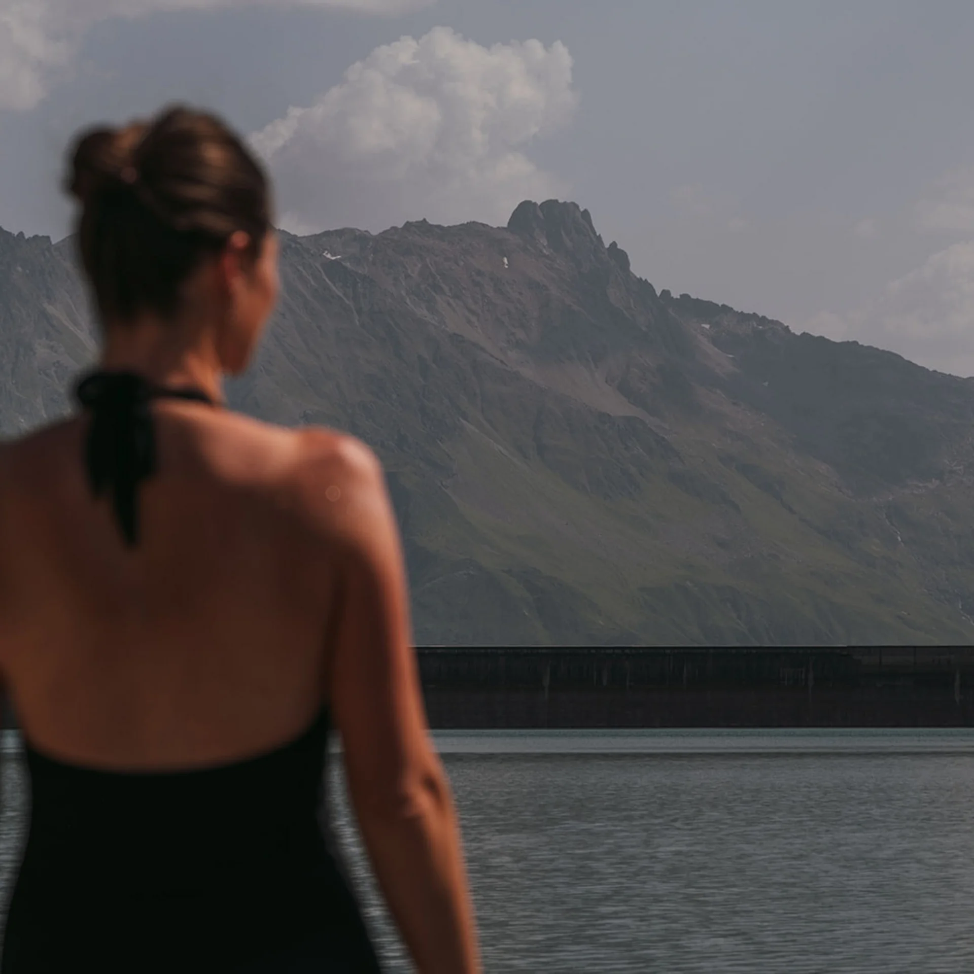 Frau blickt auf einen See mit Bergen im Hintergrund
