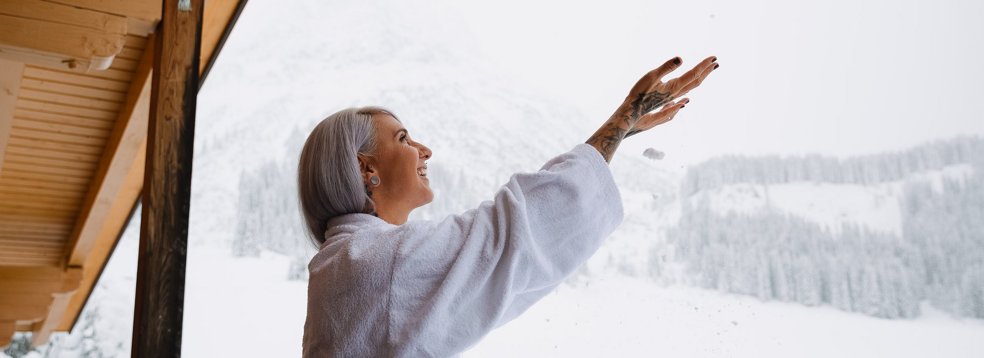 Frau im Bademantel steht am Balkon und spielt mit Schnee. 