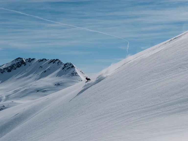 Skifahrer fährt eine steile schneebedeckte Bergabfahrt unter blauem Himmel