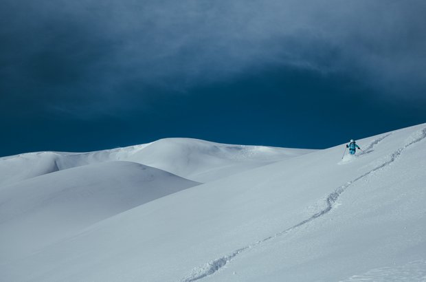 Blauer Himmel, schneebedeckte Landschaft und ein Skifahrer am wedeln. 