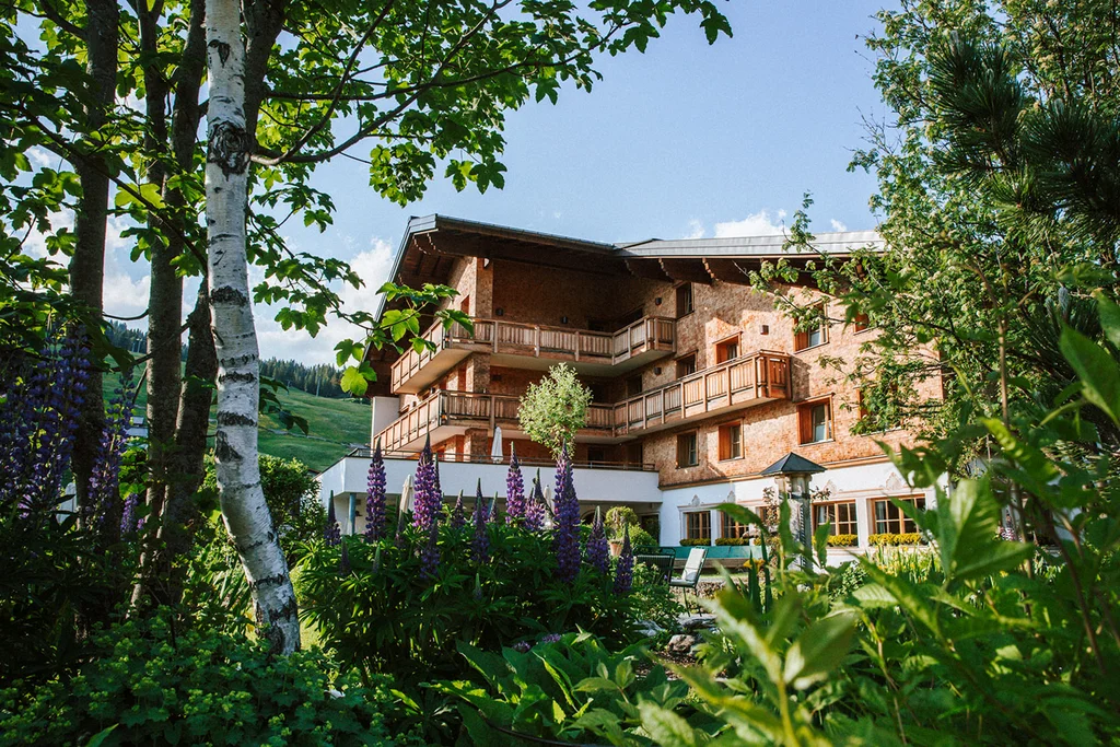 Alpenhotel mit Balkon und Garten im Grünen unter blauem Himmel