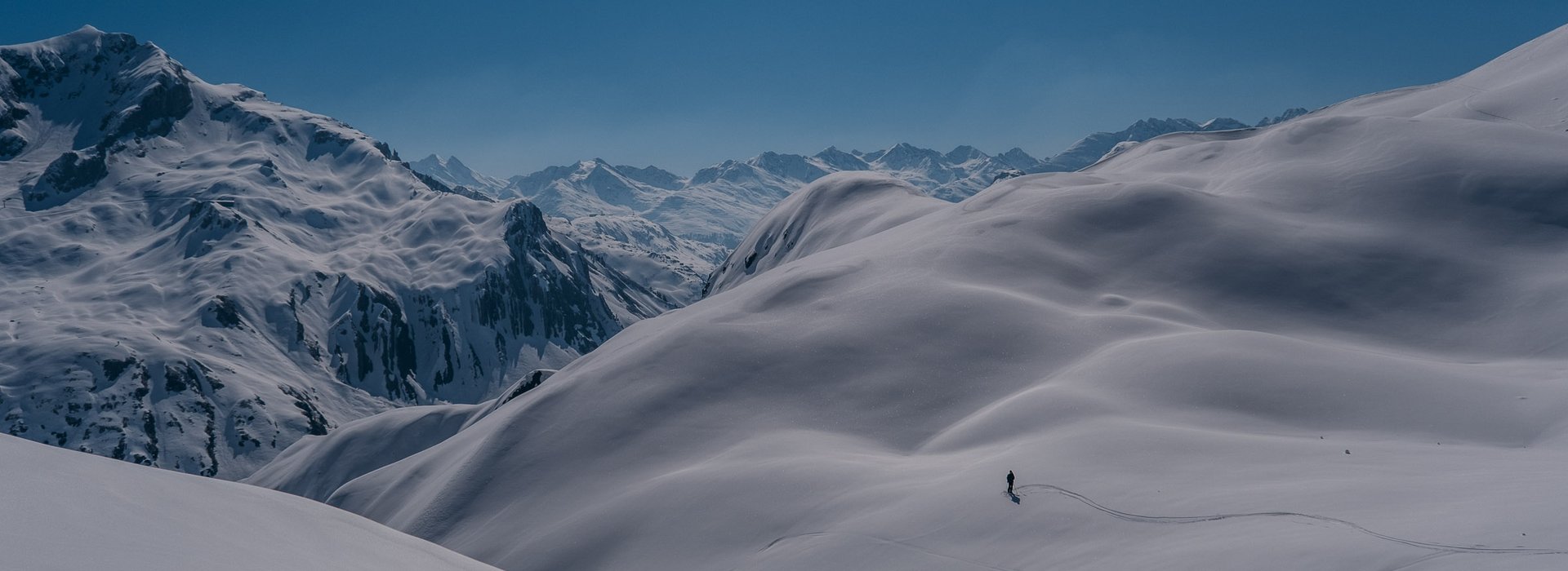 Ein einziger Skifahrer steht in mitten eines weiten schneebedeckten Bergpanoramas. 