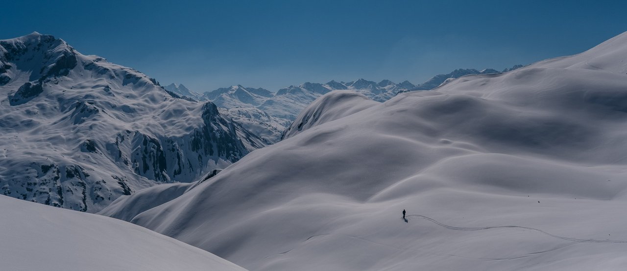 Skifahren in Lech Ein einziger Skifahrer steht in mitten eines weiten schneebedeckten Bergpanoramas.