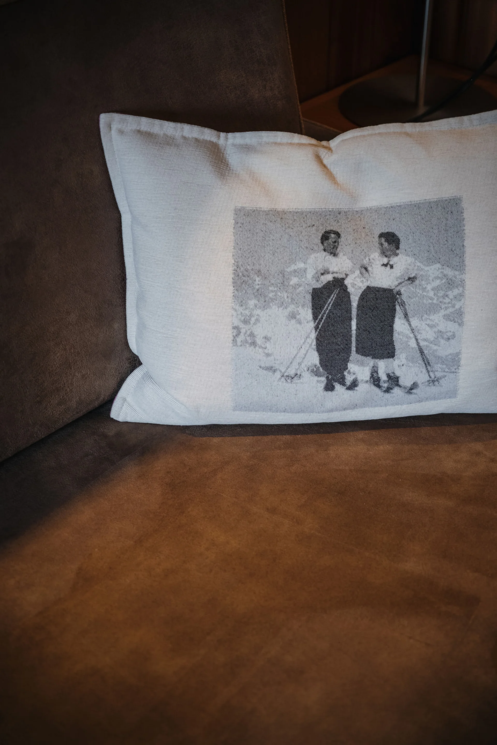 Kissen mit Bild von zwei Frauen in altertümlicher Kleidung auf braunem Sofa