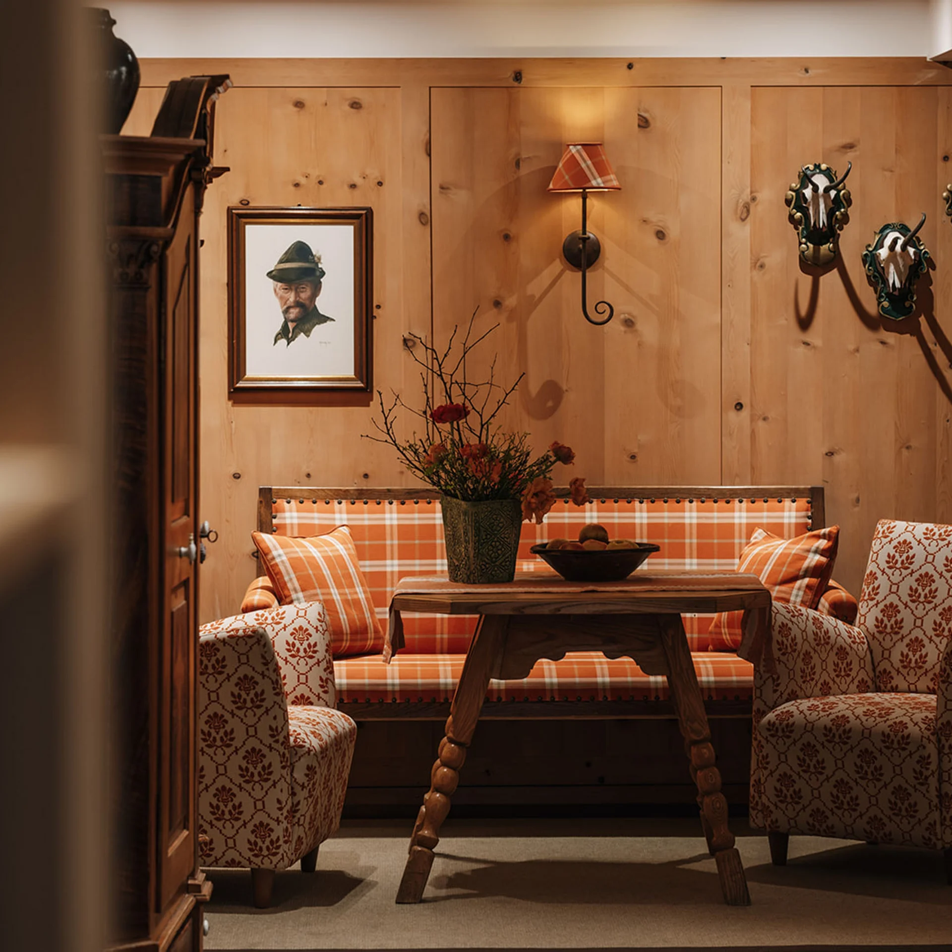 Gemütliche Sitzecke mit Holzvertäfelung, karierten Polstern und Jagdtrophäen an der Wand