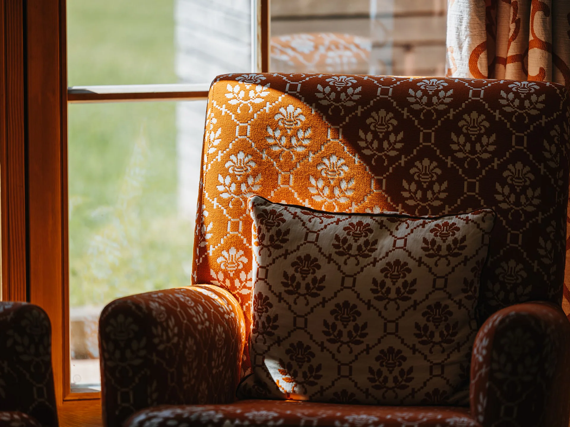 Orange armchair with patterned cushion beside window showing greenery outside