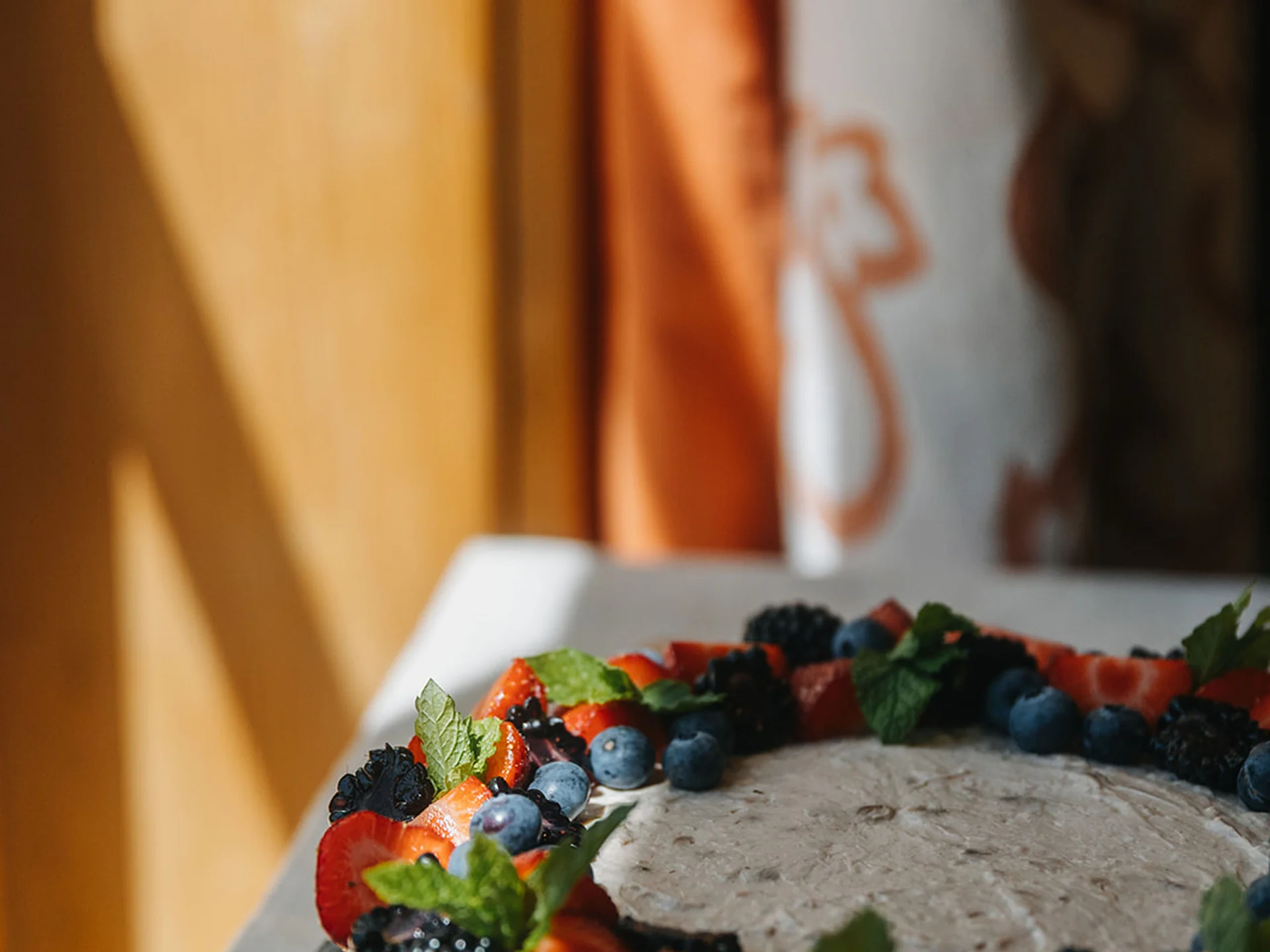 Cheesecake topped with berries and mint leaves on a table in sunlight