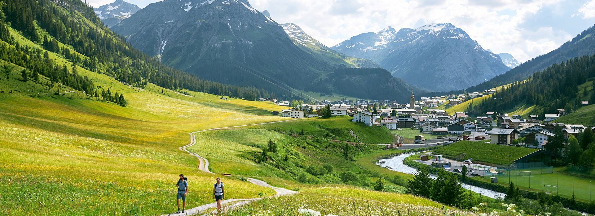 Zwei Wanderer auf dem Lechweg. Wiesen sind neben dem Weg und im Hintergrund befinden sich die Berge.