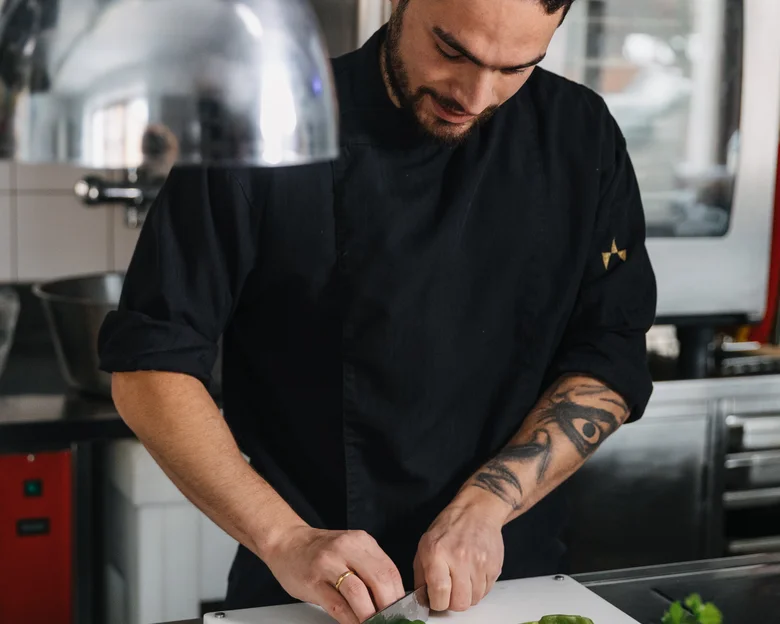 Das Team des Hotel Aurora in Lech Koch schneidet grüne Paprika in professioneller Küche