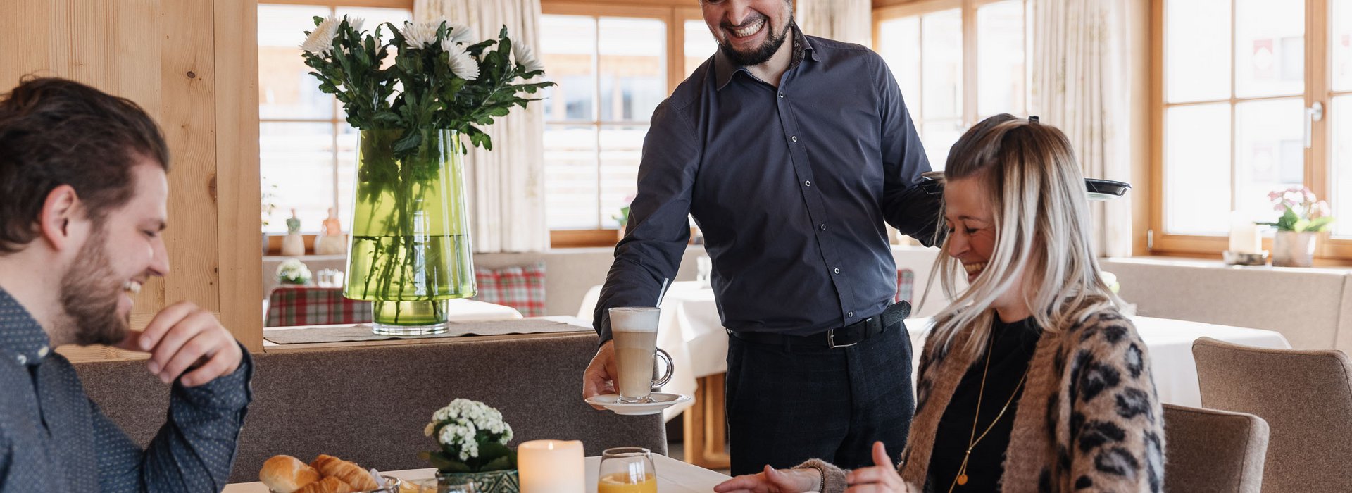 Familie sitzt beim Frühstück und der Kellner bringt einen Kaffee