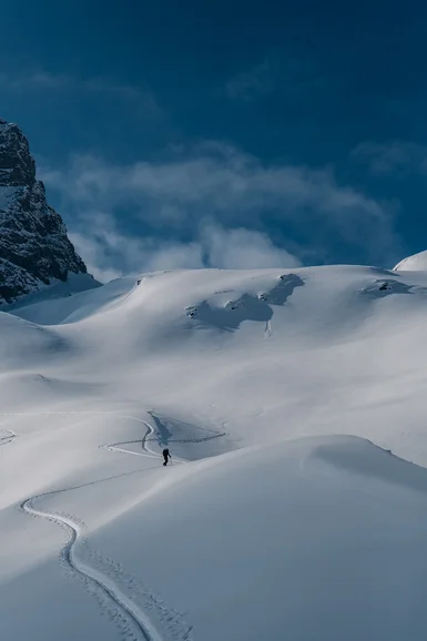 Person wandert allein durch verschneite Berglandschaft unter blauem Himmel