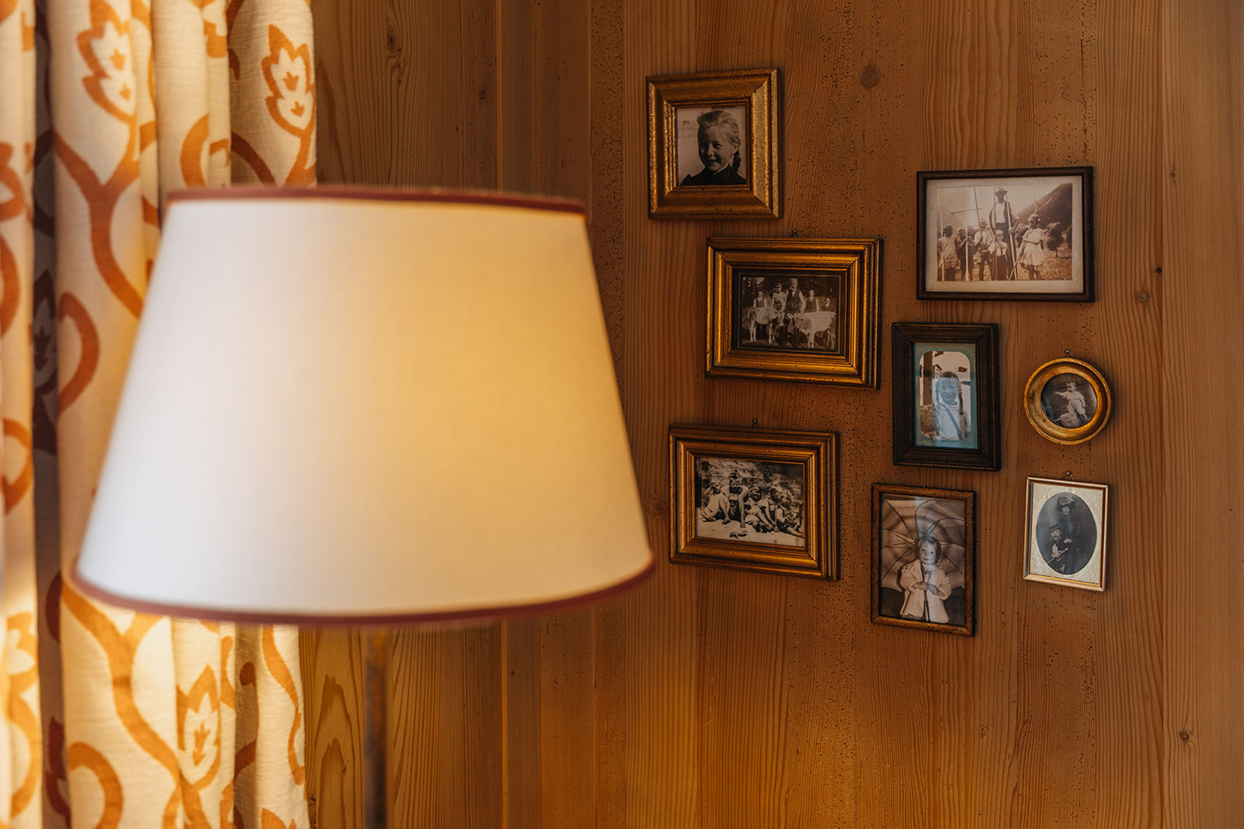 Stehlampe vor einer Holzwand mit mehreren alten Familienfotos in Rahmen