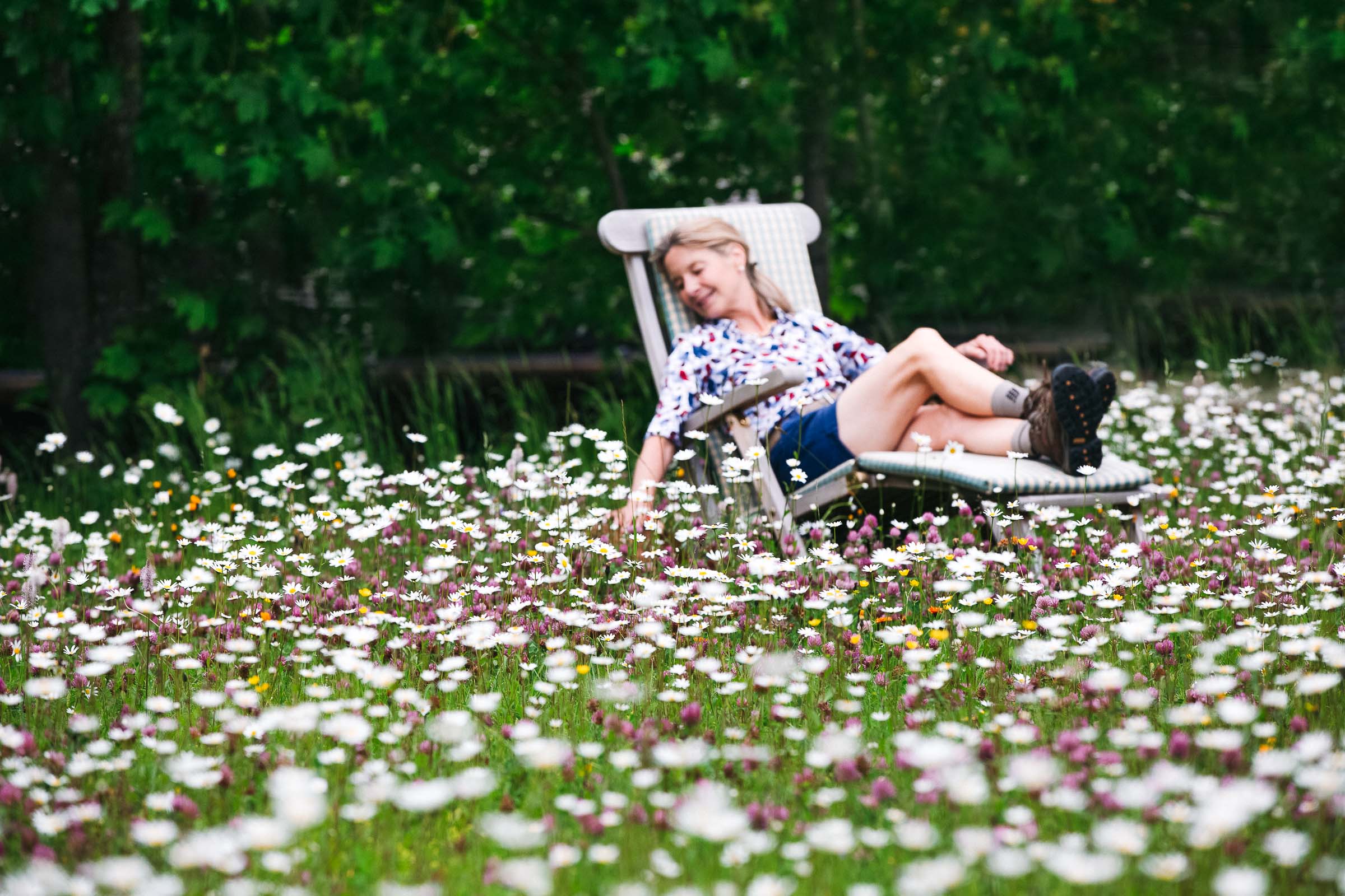 Dame liegt am Liegestuhl in einer Blumenwiese