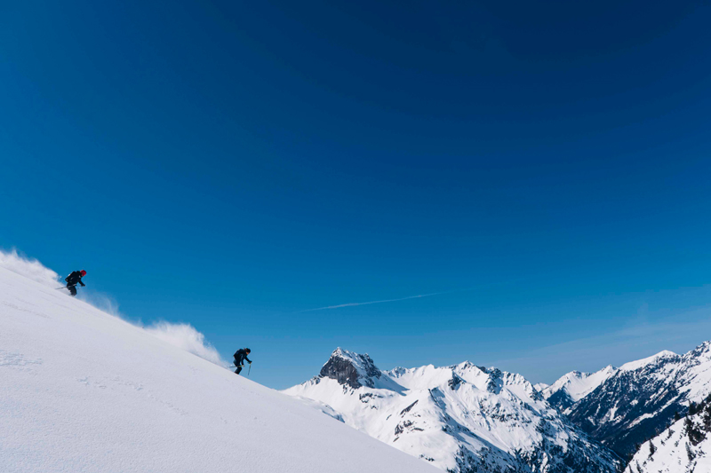 Zwei Skifahrer fahren einen verschneiten Hang hinunter