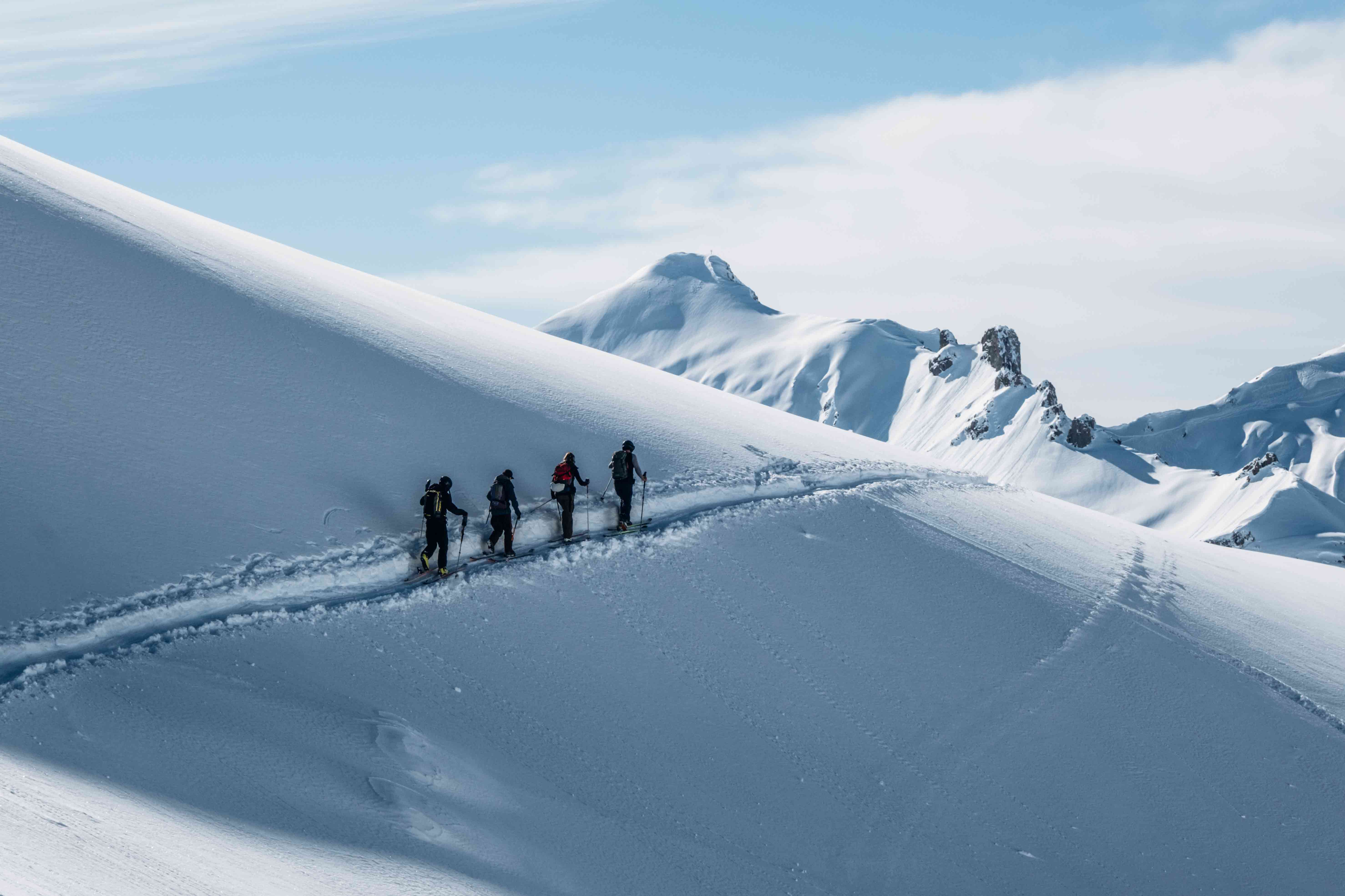 Vier Skifahrer gehen durch den Tiefschnee auf den Berg hinauf